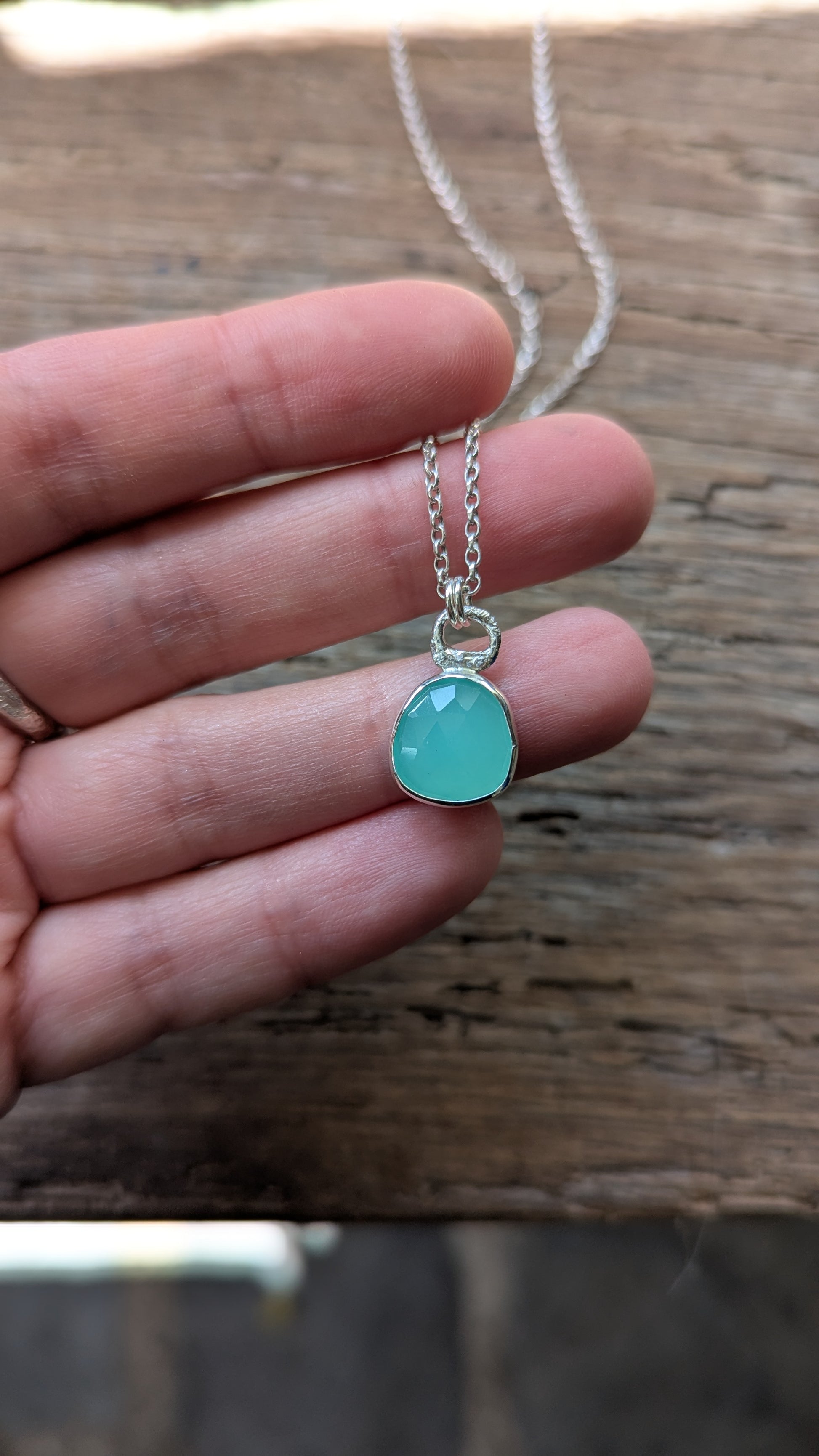 Turquoise coloured pendant necklace held in a hand against a wooden background